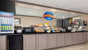 A breakfast counter with a vending machine, a microwave, and various food items. - Baymont by Wyndham Monroe (Monroe)