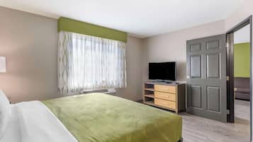 A hotel room with a bed, a TV, a desk, and a door leading to another room.