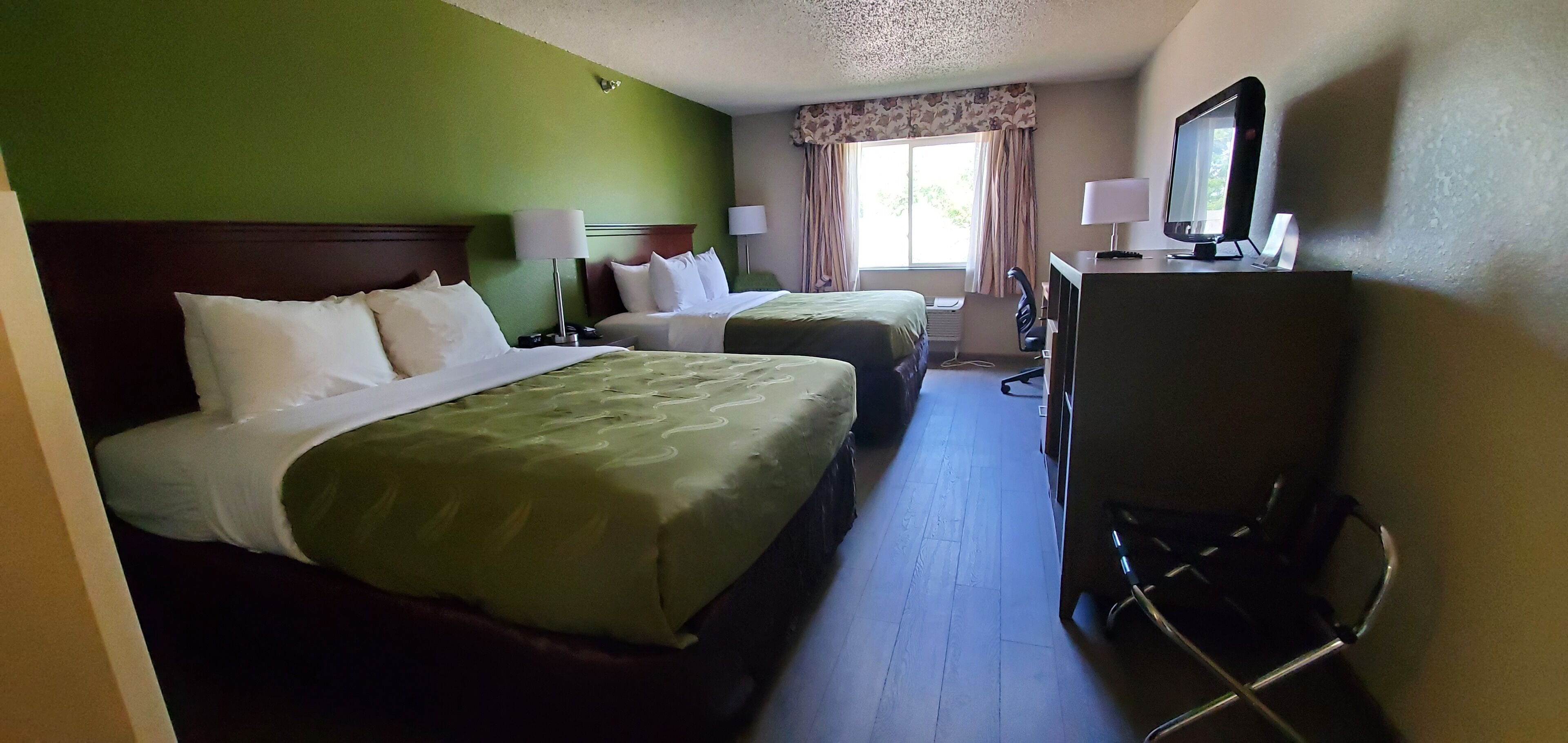 A hotel room with two beds, a television, a desk, and a chair.