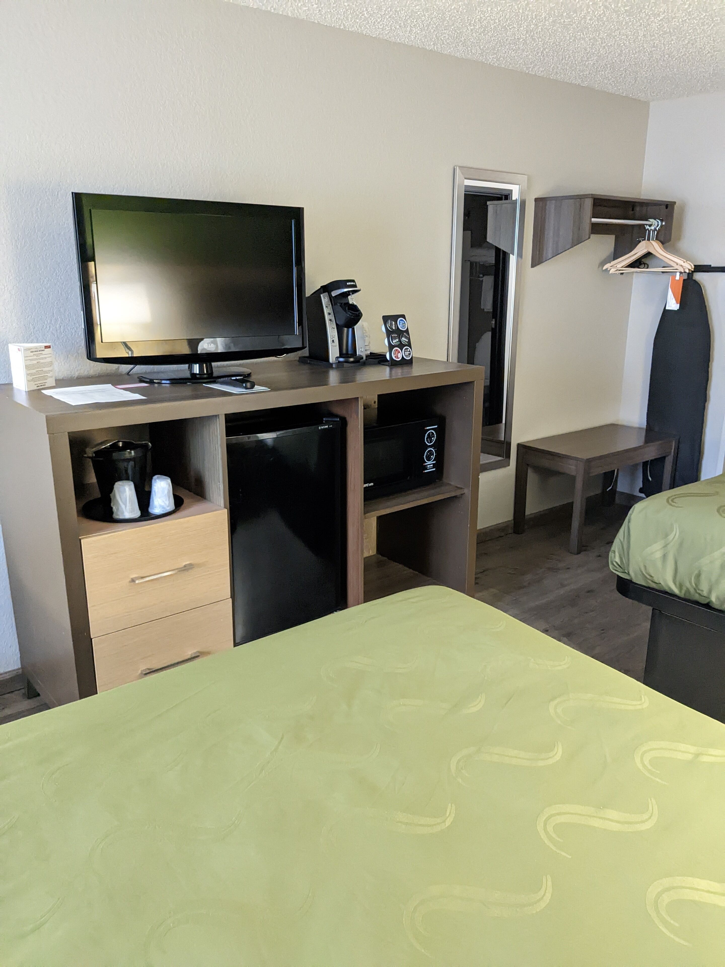 A hotel room with a bed, a desk with a television, a coffee maker, and a small refrigerator.