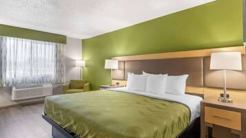 A hotel room with a large bed, two bedside tables with lamps, a green accent wall, and a window with sheer curtains.