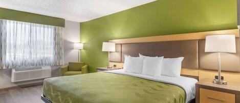 A hotel room with a large bed, two bedside tables with lamps, a green accent wall, and a window with sheer curtains.