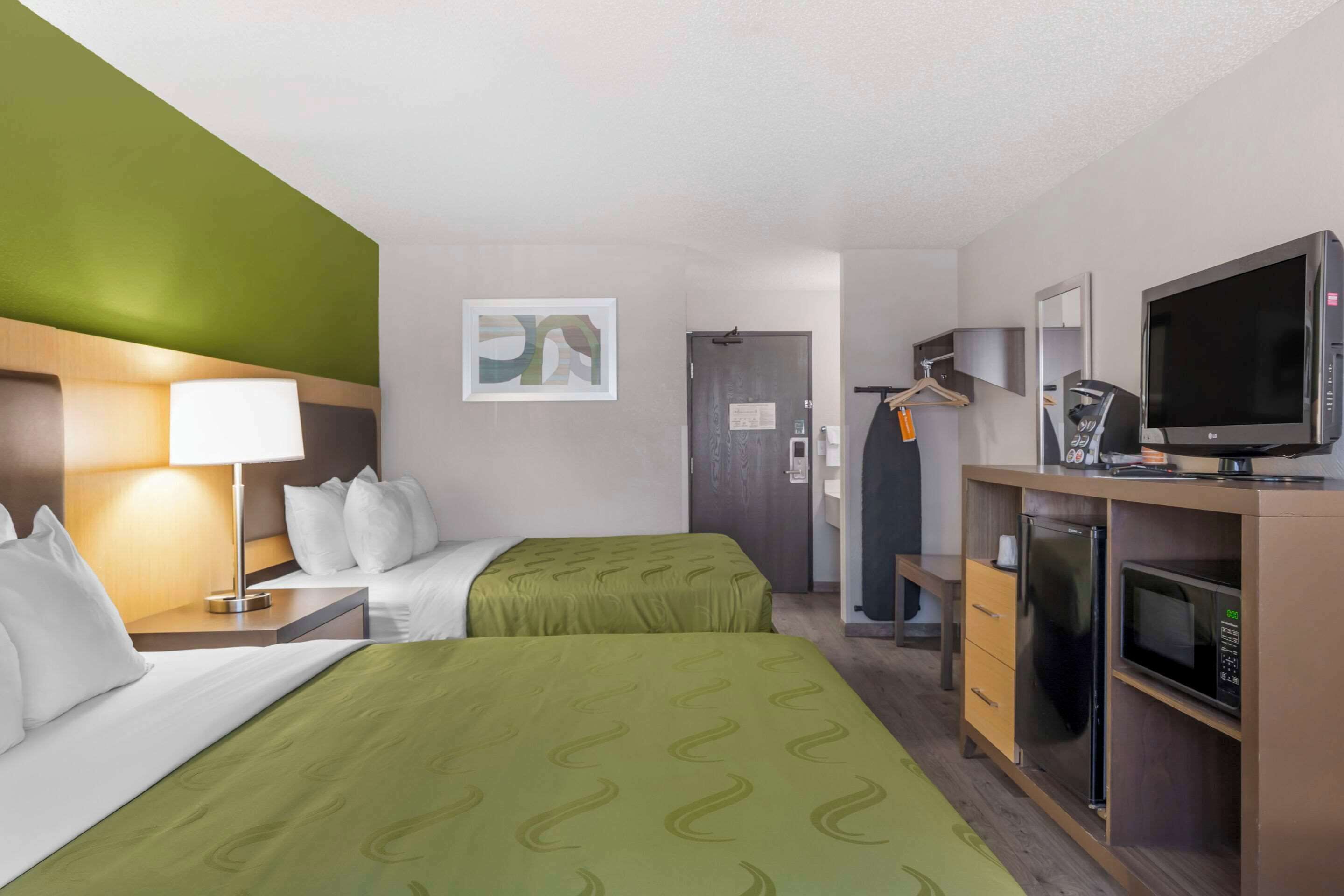 Habitación de hotel con dos camas, un escritorio con lámpara, televisor, microondas y refrigerador.