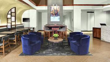 A modern lobby with a central round table, blue armchairs, and a flat-screen TV mounted on the wall.