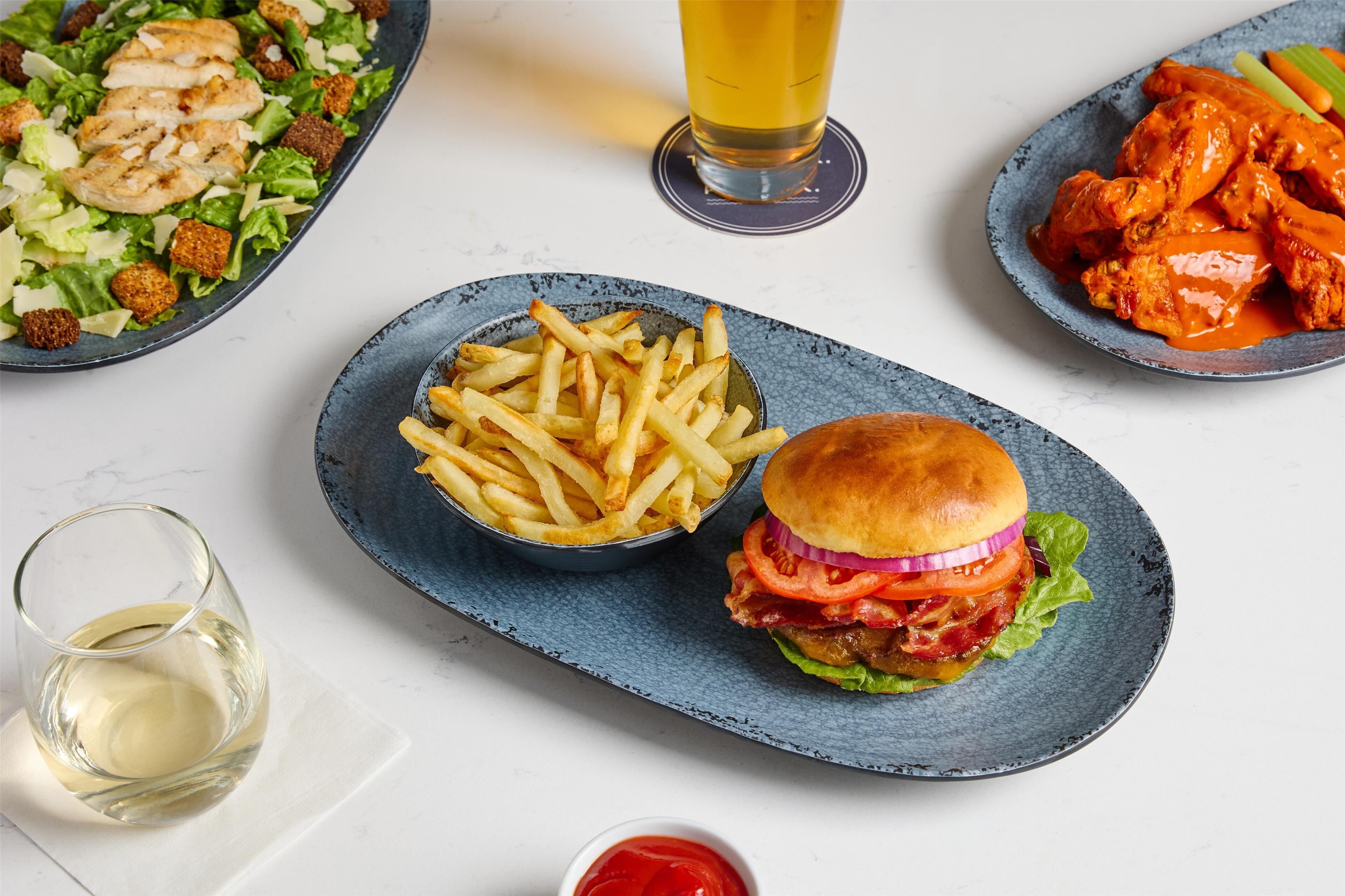 Un plato con hamburguesa, papas fritas, ensalada y alitas.