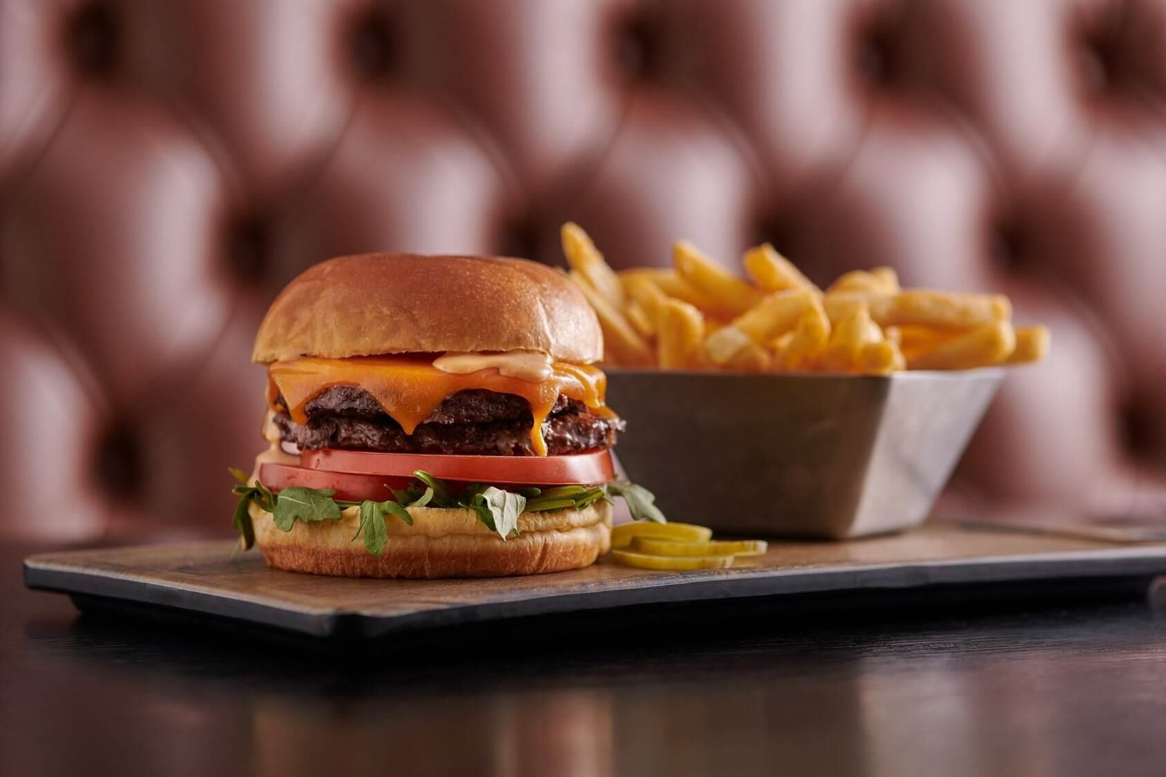 A burger with fries on a wooden board.