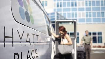 Uma carrinha branca com a inscrição "HYATT PLACE", estacionada em frente a um edifício com grandes janelas.