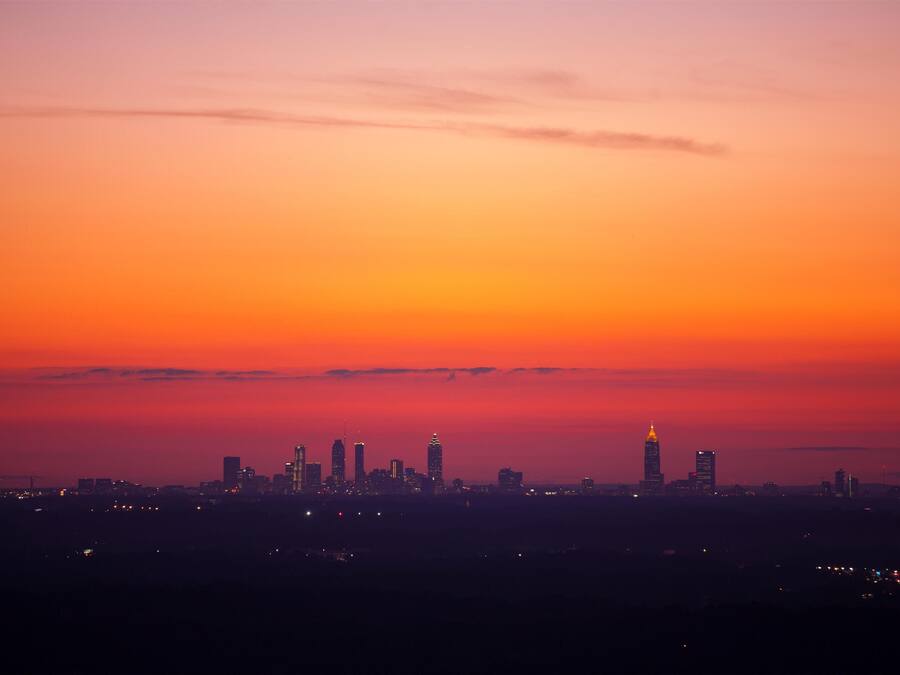 Un horizonte urbano al atardecer con edificios iluminados sobre un cielo degradado.
