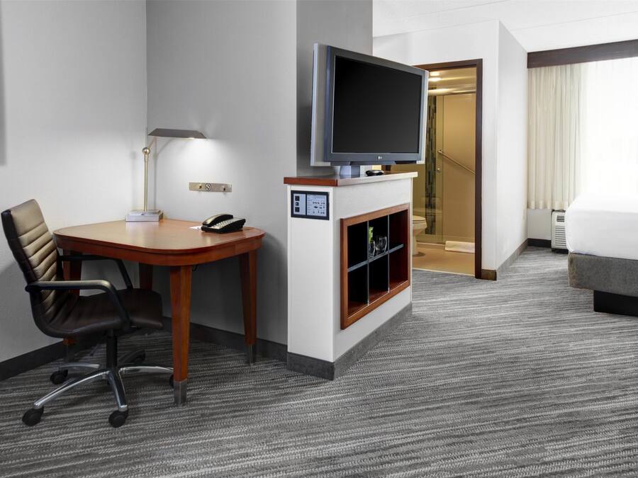 A hotel room with a flat-screen TV, a desk with a chair, a fireplace, and a bed.