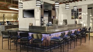 Una zona de bar moderna con una isla central, taburetes de bar, un televisor de pantalla plana y una pizarra de menú.