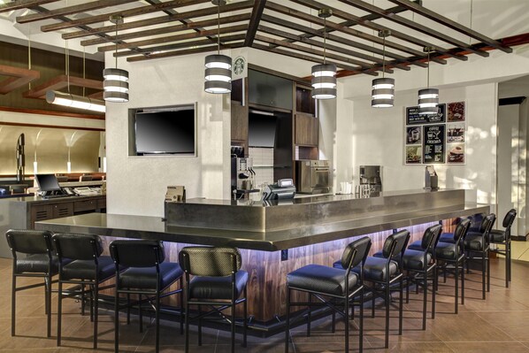 Una zona de bar moderna con una isla central, taburetes de bar, un televisor de pantalla plana y una pizarra de menú.