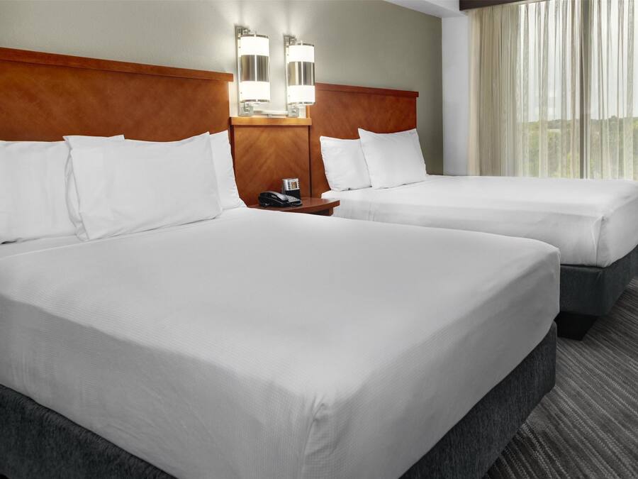 A hotel room with two beds, a wooden headboard, bedside lamps, a telephone, and a window with curtains.
