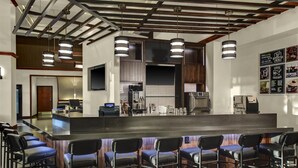 Un área de bar moderna con una barra larga, varios taburetes y luces colgantes.