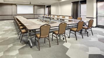 A conference room with a long table, chairs, a projector screen, and a large window with blinds.