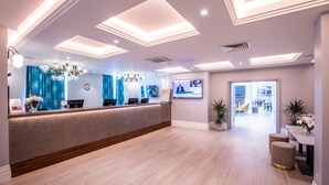 A modern reception area with a reception desk, a chandelier, and a digital screen displaying information.