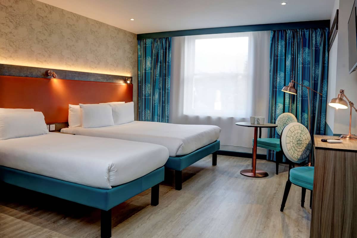 A hotel room with two beds, a desk, a chair, and a window with curtains.