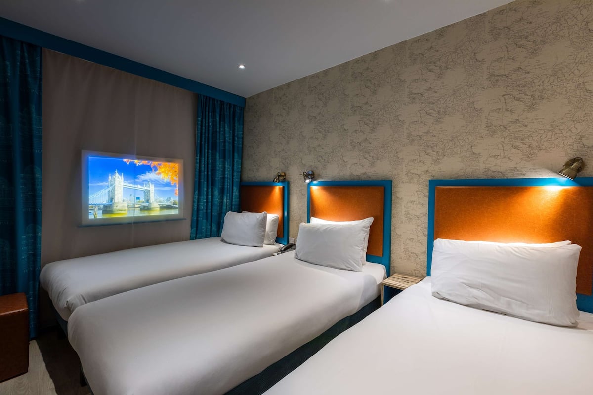 A hotel room with two single beds, a nightstand, a wall-mounted TV, and a patterned wallpaper.