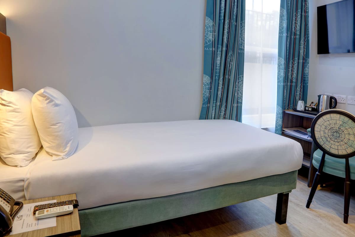 A neatly made bed with white linens, a bedside table with a telephone and a notepad, and a chair with a patterned backrest.