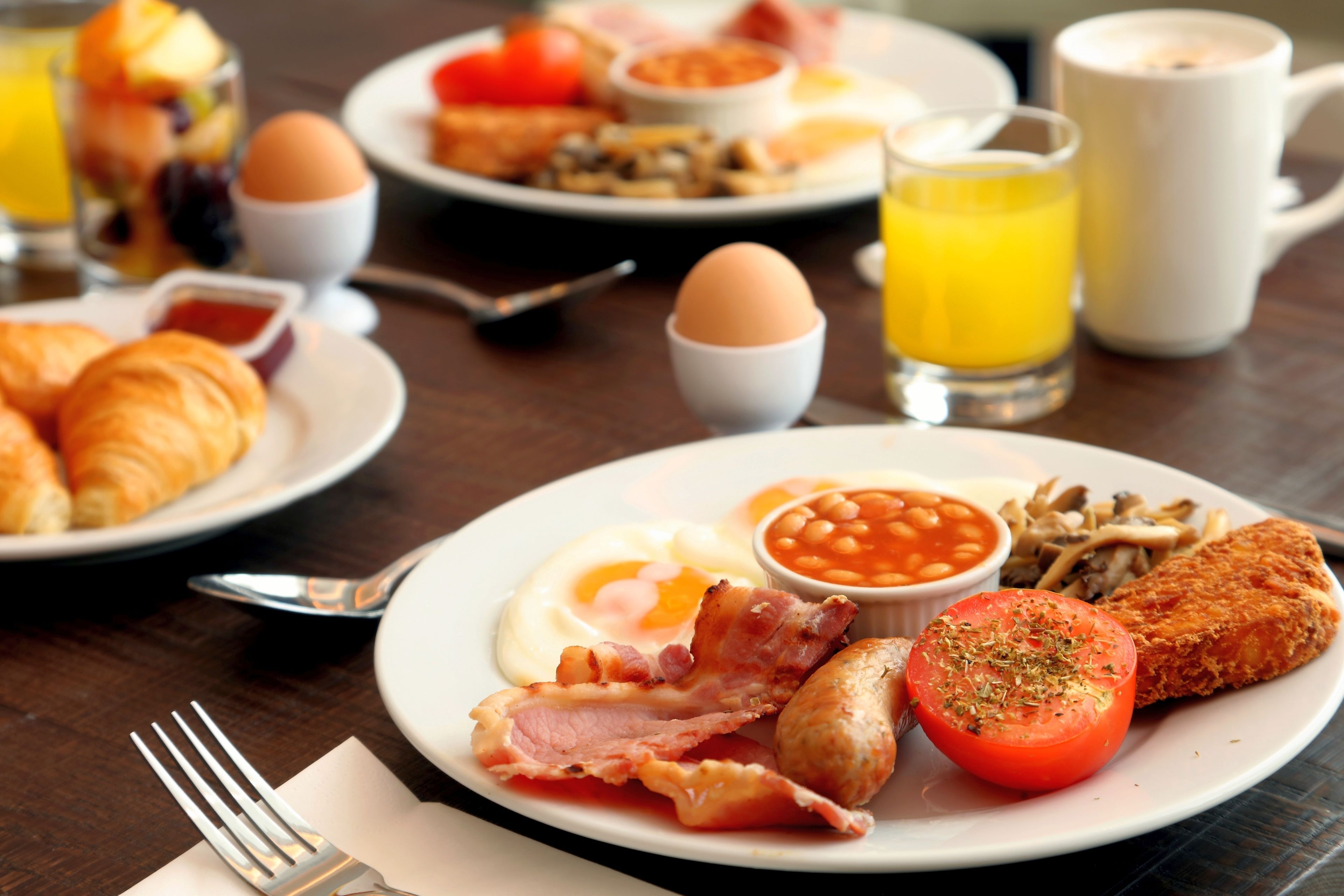 A breakfast table with plates of eggs, bacon, sausages, and toast.