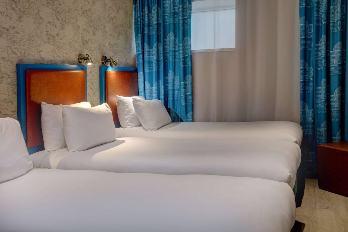 A hotel room with two beds, a wooden headboard, white bedding, and blue curtains with a pattern.