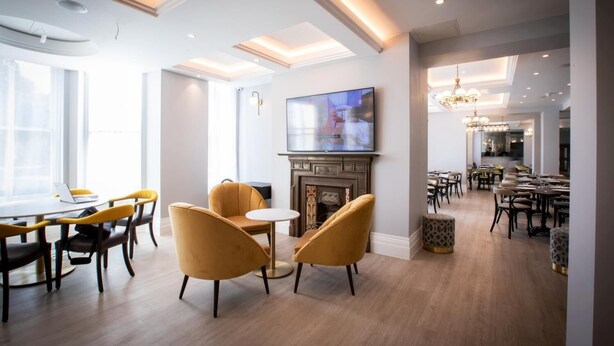 A modern hotel lobby with a fireplace, a television, and a dining area.