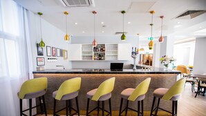 A modern bar area with a counter, bar stools, hanging pendant lights, and a display of bottles and glasses.