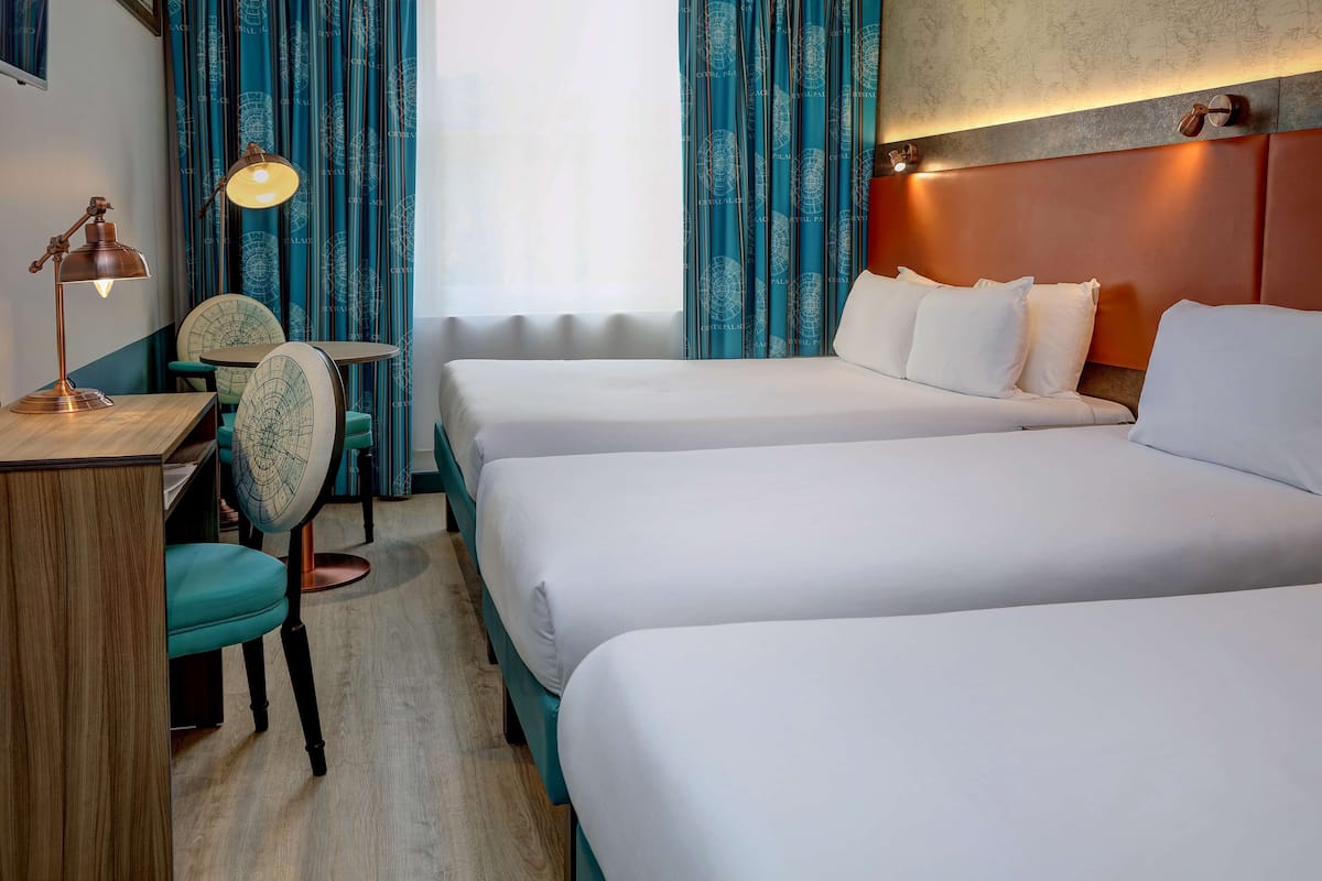 A hotel room with two beds, a desk, a chair, and a lamp.