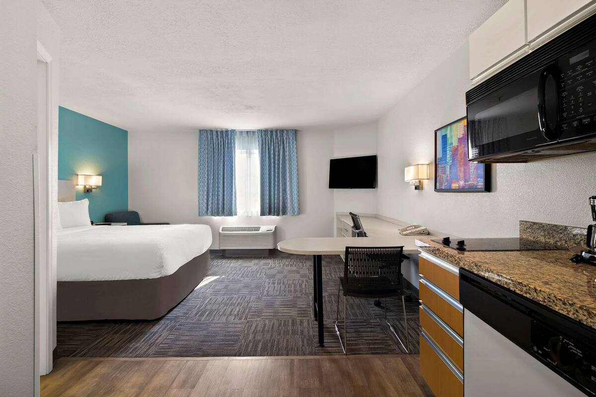 Une chambre d’hôtel avec un lit, un bureau, un four à micro-ondes, une télévision et un tableau au mur.