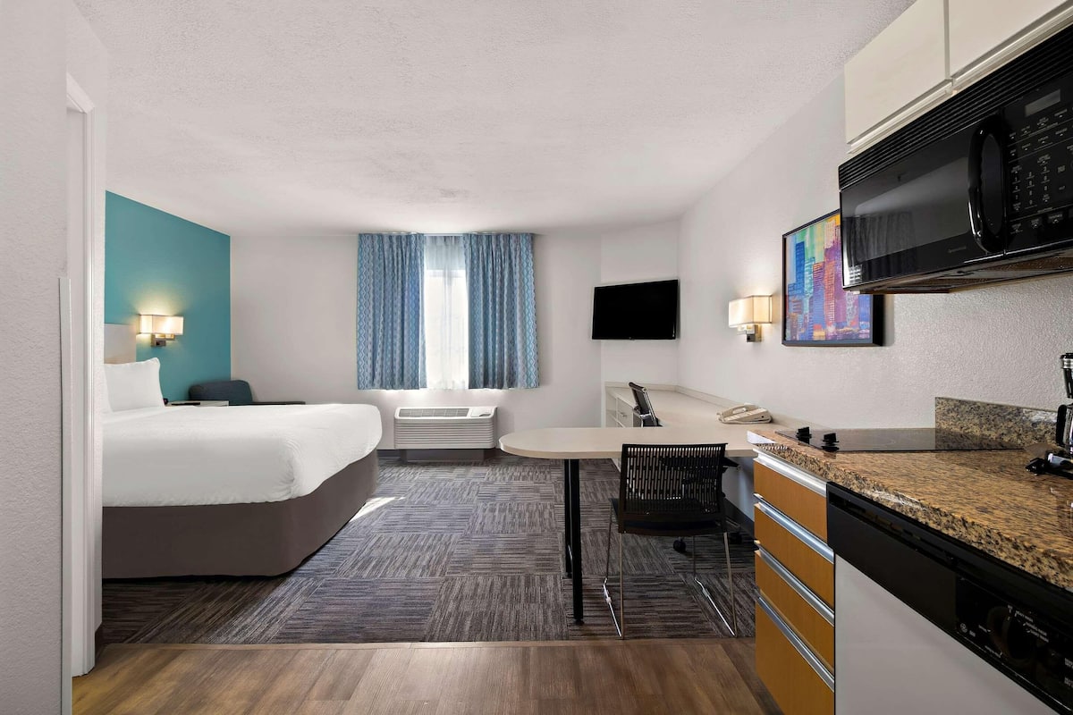 Ein Hotelzimmer mit Bett, Schreibtisch, Mikrowelle, Fernseher und einem Bild an der Wand.