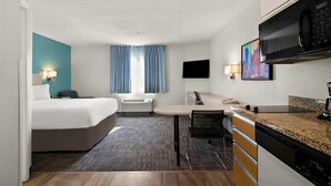 Una habitación de hotel con cama, escritorio, microondas, televisión y un cuadro en la pared.