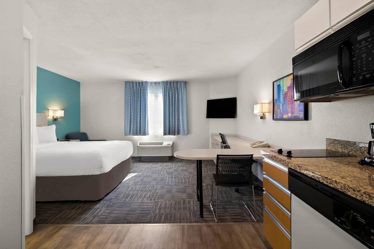 Une chambre d’hôtel équipée d’un lit, d’un bureau, d’un four à micro-ondes, d’une télévision et d’un tableau au mur.