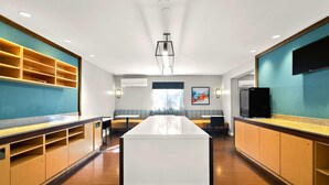 Una habitación de hotel moderna con una isla central, estanterías empotradas, un televisor de pantalla plana y un ventanal grande.
