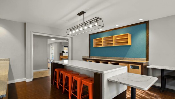 Cocina moderna con una isla blanca, taburetes de bar naranjas, una pared de acento azul y una lámpara colgante.