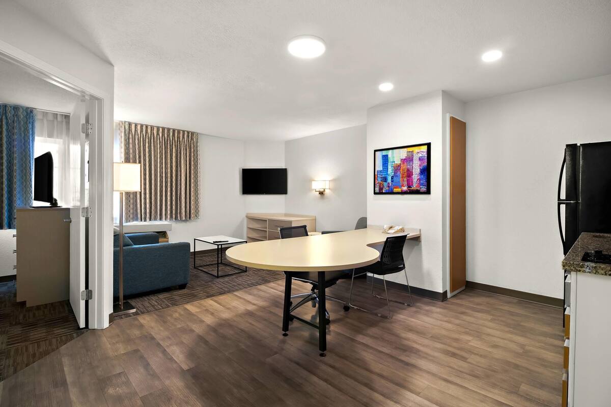 Une chambre d’hôtel moderne équipée d’une table ronde, d’un canapé, d’un téléviseur à écran plat et d’un réfrigérateur.