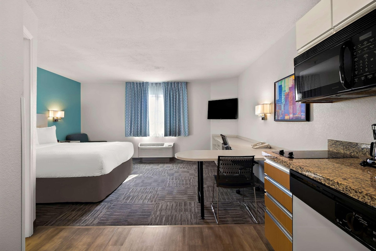 Habitación de hotel con cama, escritorio, microondas, televisor y un cuadro en la pared.