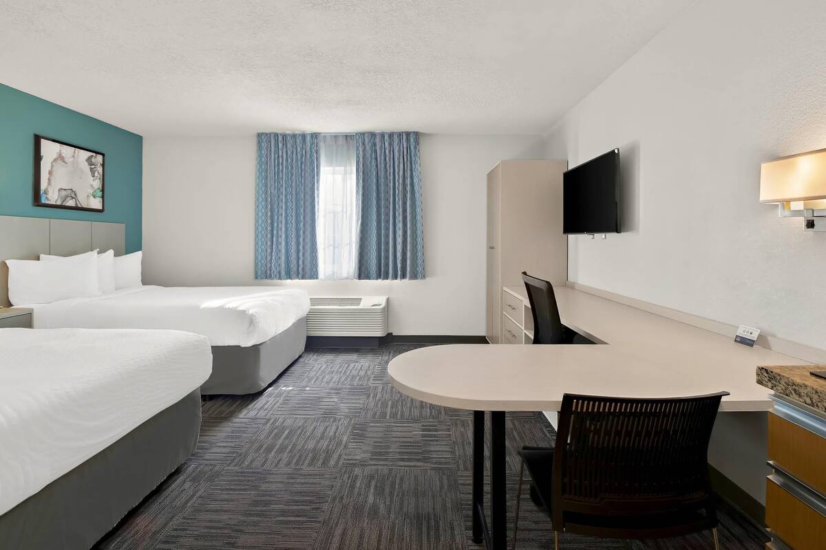 Une chambre d’hôtel avec deux lits, un bureau, une chaise, une télévision et une fenêtre avec des rideaux.