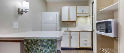 A compact kitchenette with a refrigerator, microwave, and wooden cabinets.