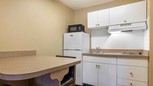 A compact kitchen with a microwave on a white refrigerator, a sink, and white cabinets.