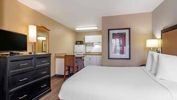 A hotel room with a bed, a desk, a chair, a television, a microwave, and a framed picture on the wall.