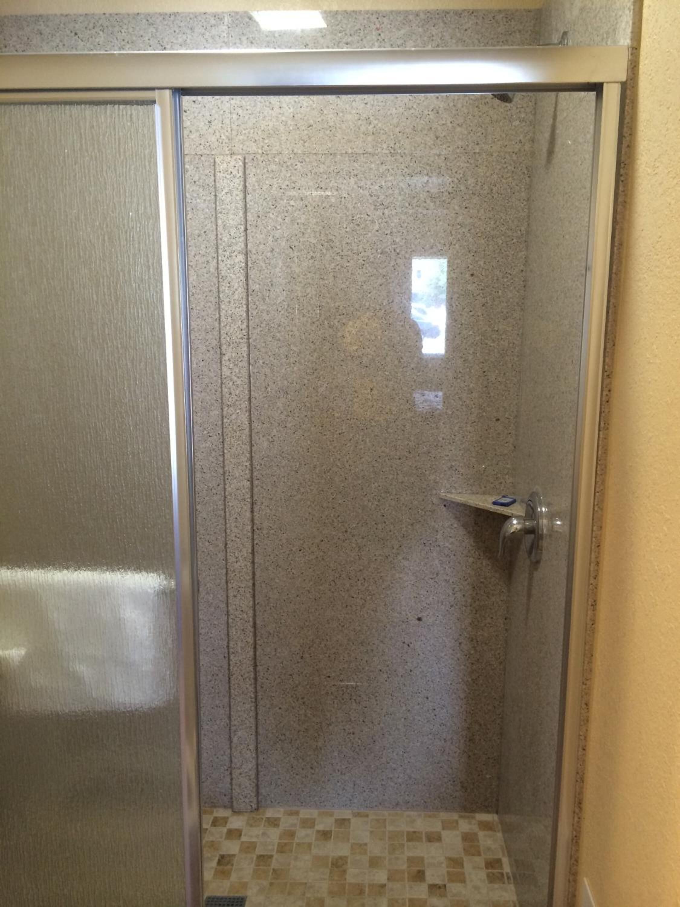A glass-enclosed shower with a tiled floor and a metal door.
