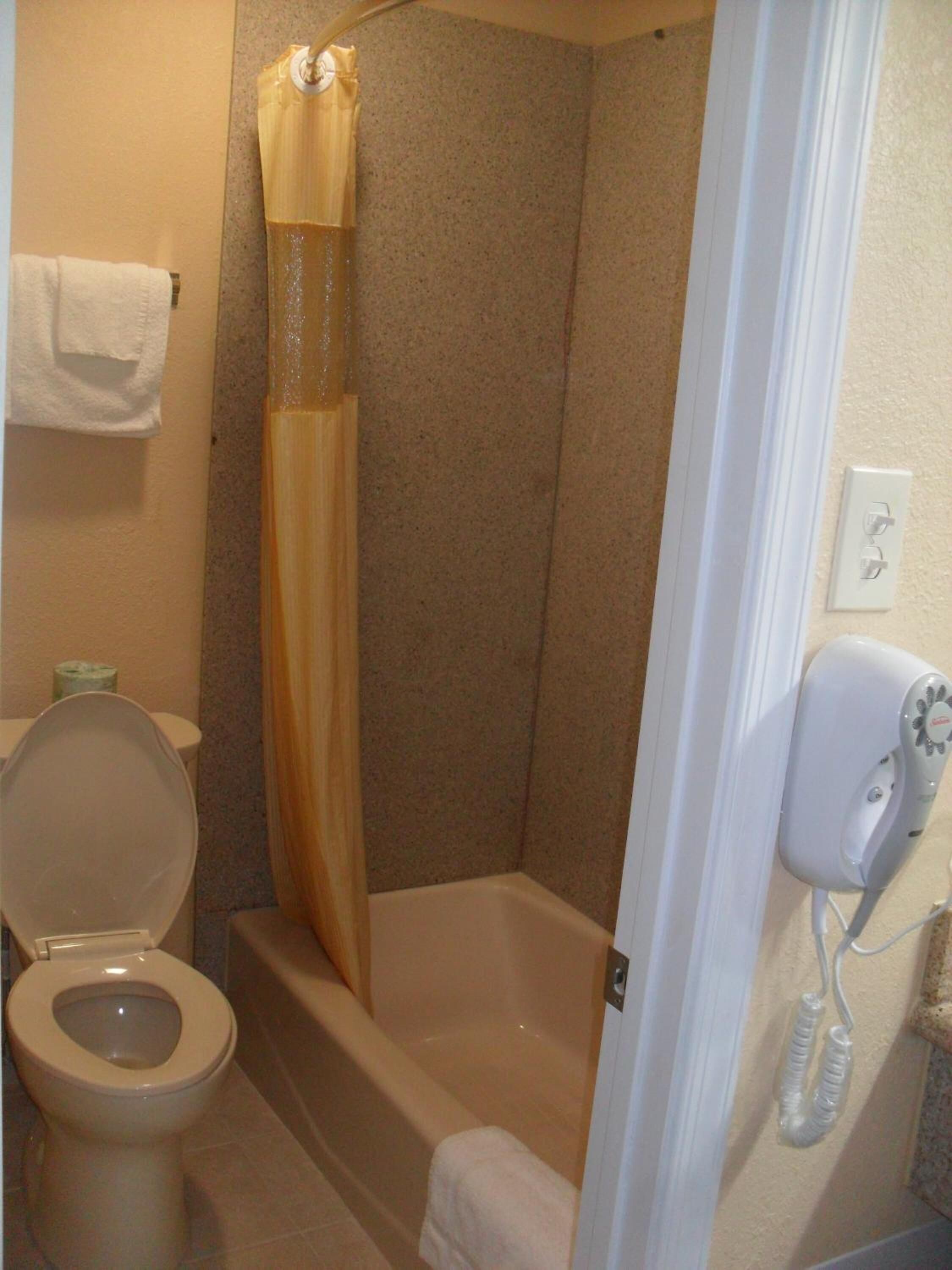 Un baño con inodoro, ducha con cortina y secador de pelo en la pared.
