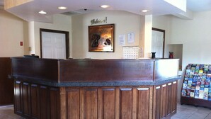 A reception desk with a wooden finish, a welcome sign, a calendar, and a display of magazines. - Newport News Inn (Newport News)