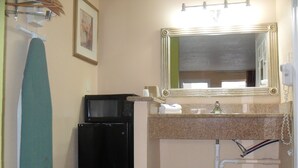 A compact bathroom with a sink, mirror, and a black appliance, possibly a microwave or coffee maker, on the countertop. - Newport News Inn (Newport News)