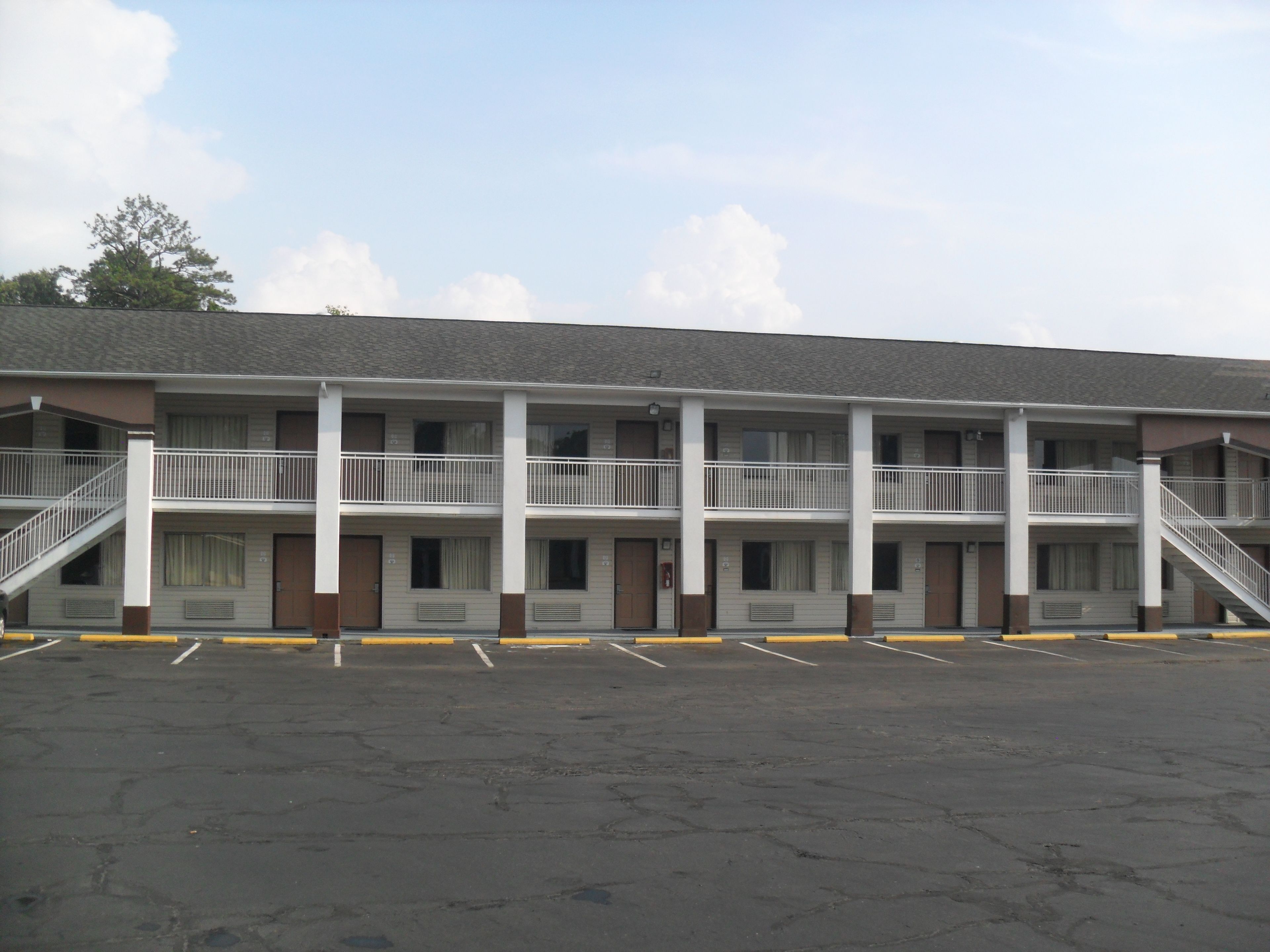 A motel with a two-story structure, multiple balconies, and a parking lot in front.