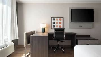 Una habitación de hotel con cama, escritorio, silla, televisor, lámpara y ventana con cortinas.