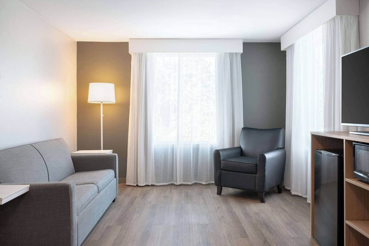 A modern living room with a grey sofa, a black armchair, a flat-screen TV, and a floor lamp.