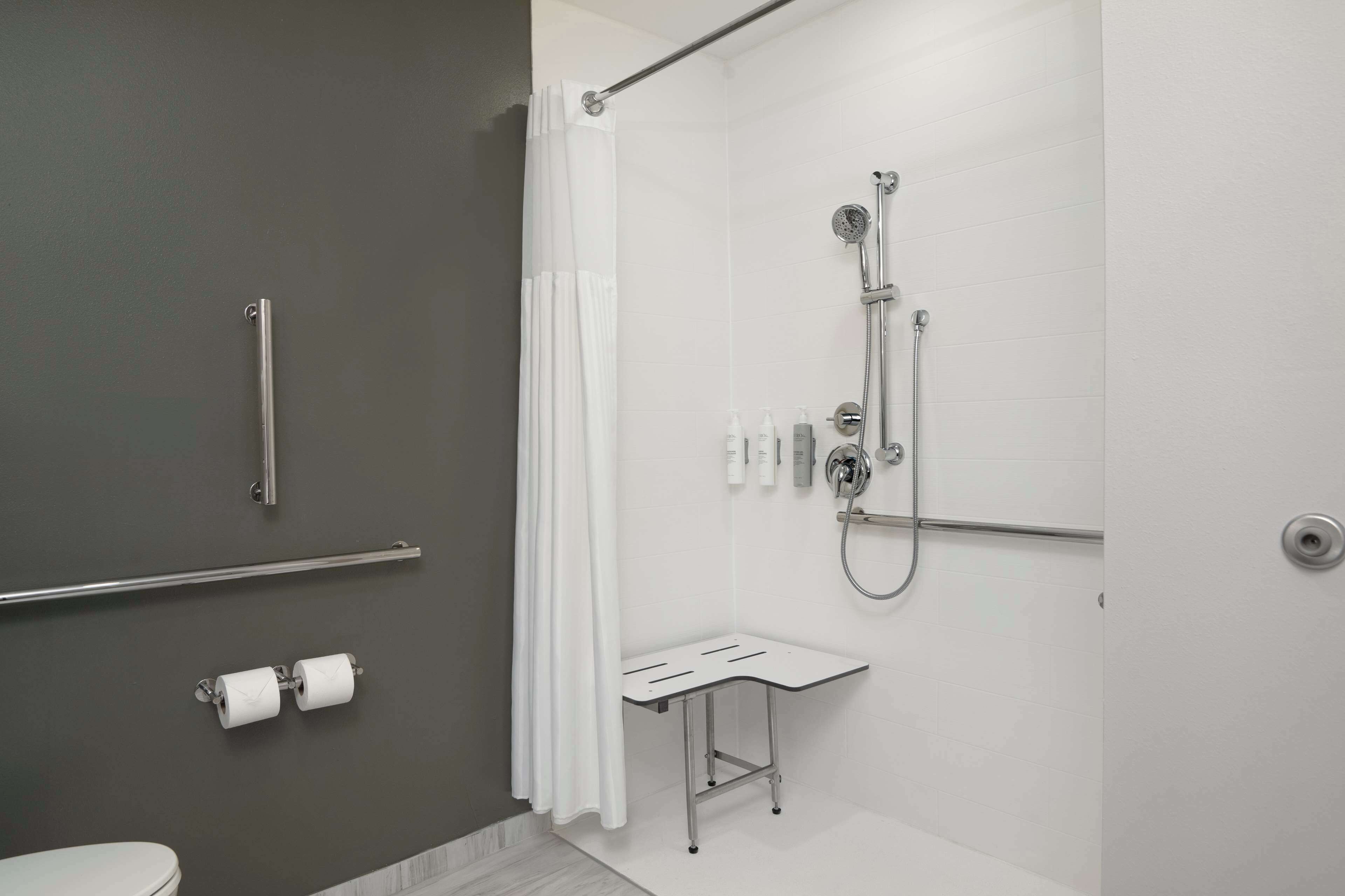A modern bathroom with a shower, toilet, and grab bars.