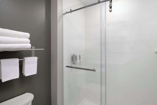 Un baño moderno con cabina de ducha de vidrio, un inodoro y un estante con toallas blancas dobladas con cuidado.
