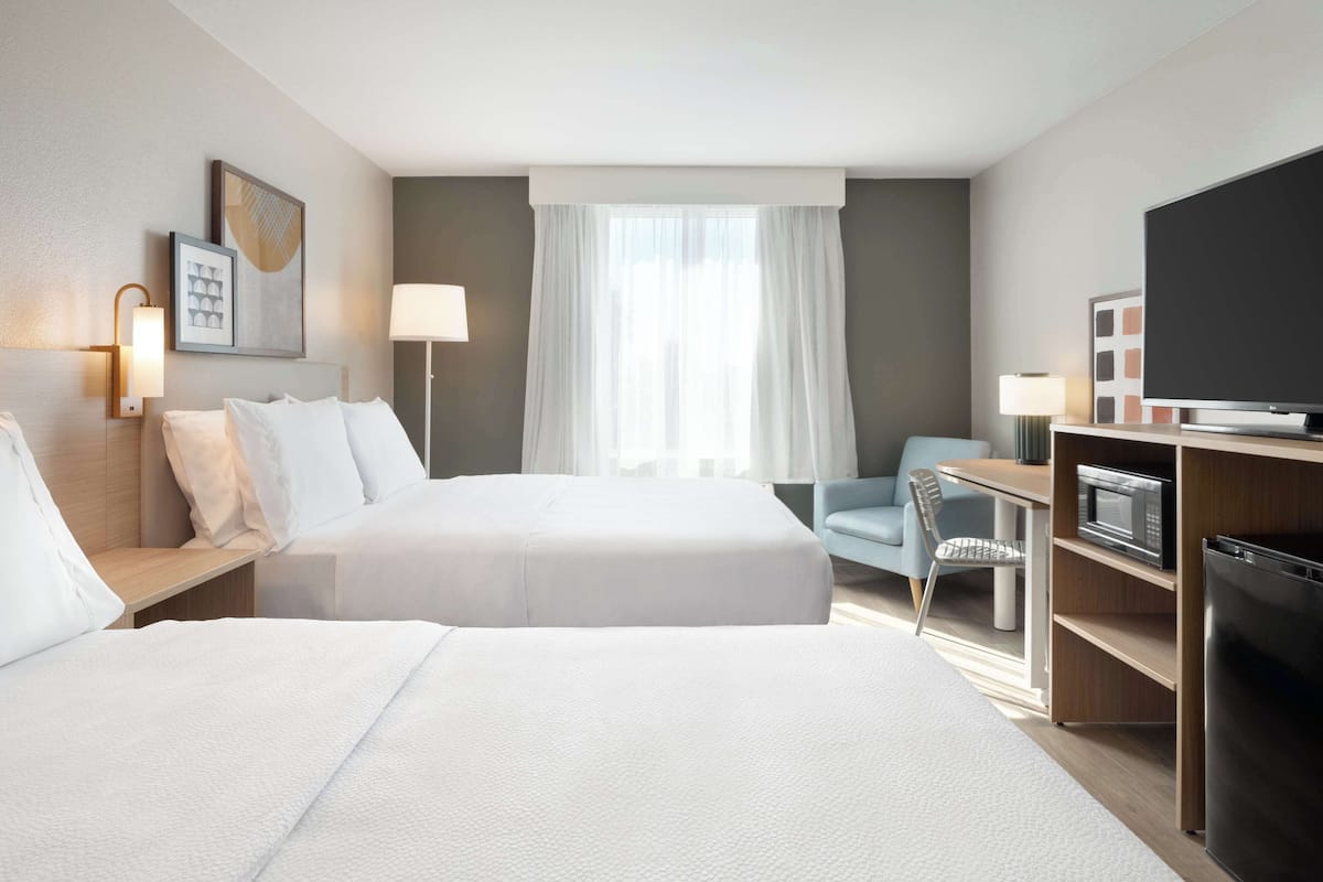 A hotel room with two beds, a desk with a chair, a TV, a microwave, and a refrigerator.