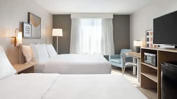 A hotel room with two beds, a desk with a chair, a TV, a microwave, and a refrigerator.